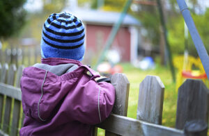 Barn som tittar över ett staket in mot en lekplats.