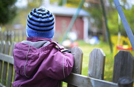 Barn som tittar över ett staket in mot en lekplats.