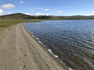 En stenstrand, vatten och i bakgrunden syns låga berg.