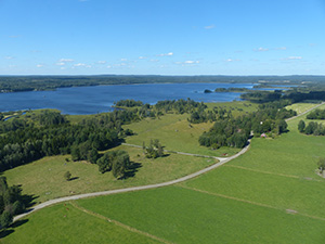 Flygfoto över åker, väg, skog och en sjö.